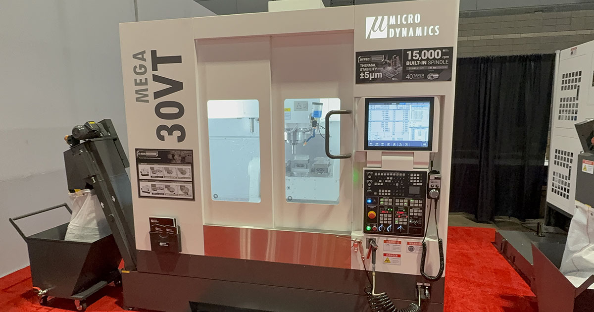 Micro Dynamics MEGA 30VT machining center displayed at IMTS 2026, with its enclosure, control and chip conveyor visible.